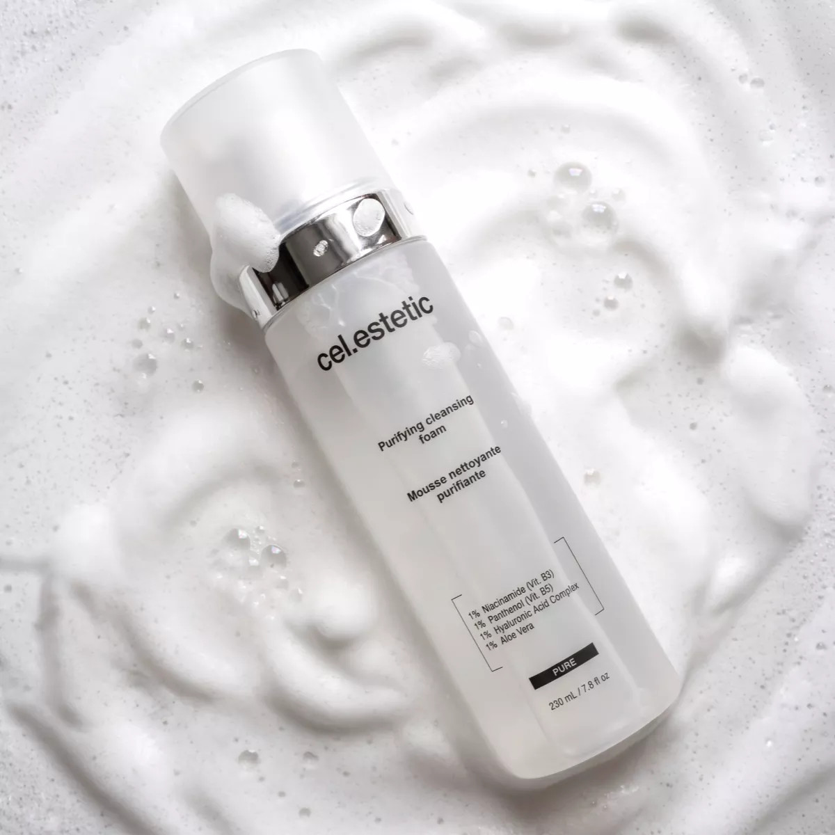 Witte fles met zilveren dop en label “cel-estetic” op schuimige, gespetterde achtergrond. Purifying Cleansing Foam